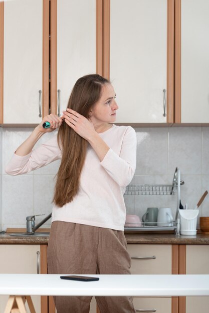 Junge Frau, die ihr Haar vor Küchenhintergrund kämmt Vertikaler Rahmen