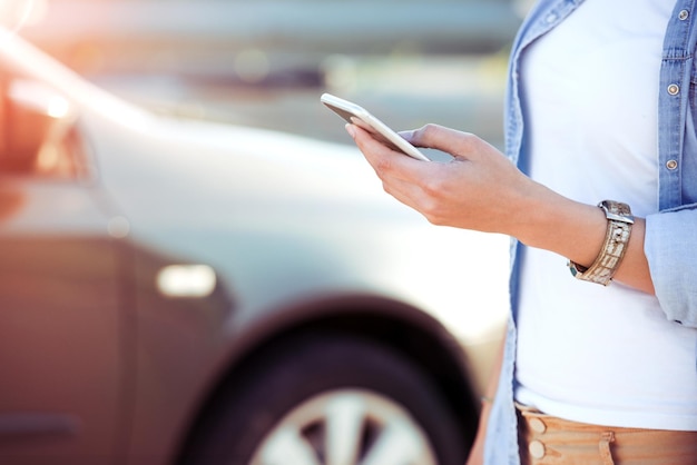 Junge Frau, die ihr Telefon auf der Straße neben ihrem Auto benutzt