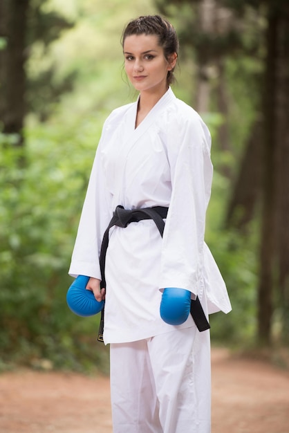 Foto junge frau, die ihre karate-bewegungen in einem bewaldeten waldgebiet übt weißer kimono schwarzer gürtel