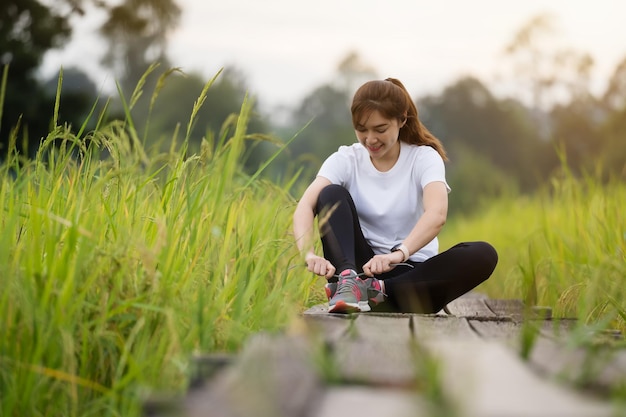 Junge Frau, die ihre Laufschuhe auf einem Holzweg im Feld bindet