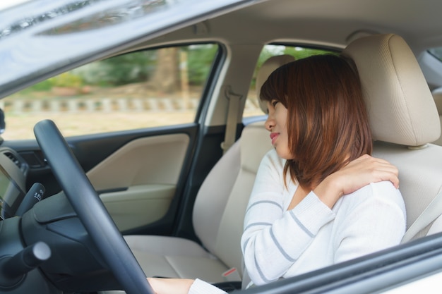 Junge Frau, die ihren Arm oder Schulter beim Fahren eines Autos nach langer Stunde massiert