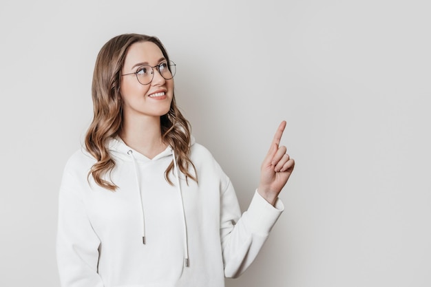 Junge Frau, die ihren Finger oben auf den Kopienraum zeigt, der auf weißem Hintergrund lokalisiert wird