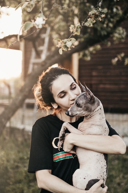 Junge Frau, die ihren geliebten haarlosen amerikanischen Terrierhund im Freien hält