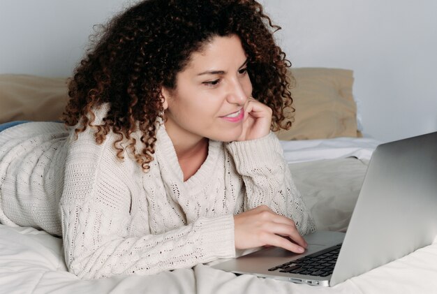 Junge Frau, die ihren Laptop auf Bett verwendet