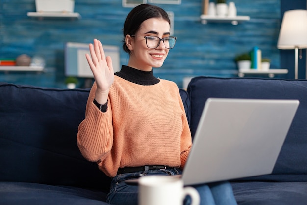 Junge Frau, die ihren Lehrer während eines virtuellen Videoanrufs begrüßt, der über das Universitätsprojekt spricht. Student im Wohnzimmer auf Online-Internet-Web-Videokonferenz Duting virtueller E-Learning-Kurs