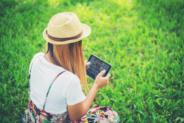 Junge Frau, die ihren Tablet-Computer bei in einem Park sich draußen entspannen verwendet.