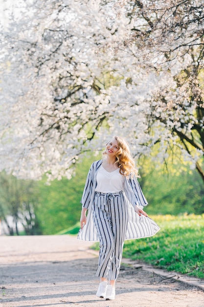 Junge Frau, die im Blumengarten lächelt. Mädchen unter Sakura-Blütenbaum. Sommermode-Konzept