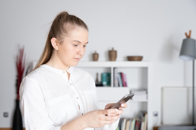 Junge Frau, die im Büro auf ihr Telefon schaut