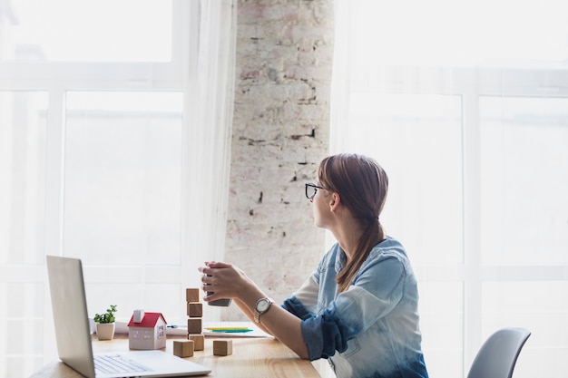 Foto junge frau, die im büro hält kaffeetasse in der hand sitzt