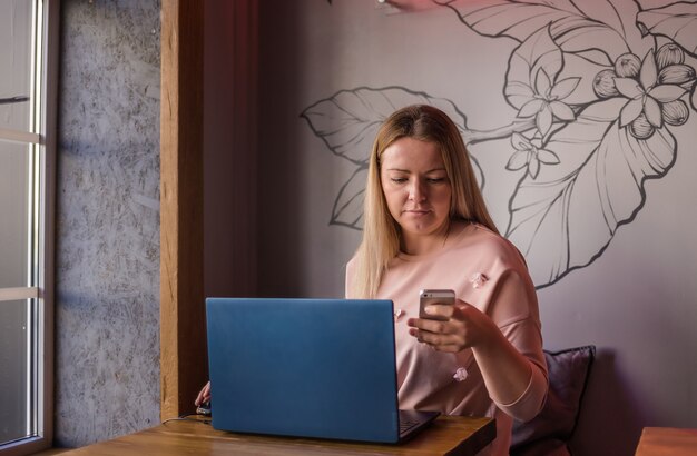 Junge Frau, die im Café mit Laptop und Telefon sitzt