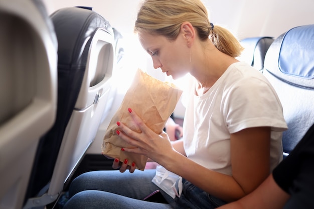 Junge Frau, die im Flugzeug fliegt und in Papiertüte atmet