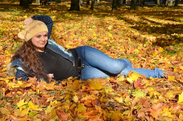 Junge Frau, die im hellen Herbstlaub liegt und lächelt