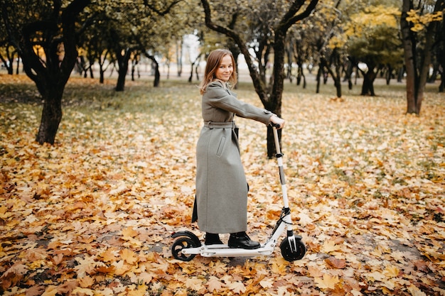 Junge Frau, die im Herbst einen Elektroroller in einem Stadtpark fährt