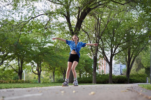 Junge Frau, die im Park mit offenen Armen auf Inline-Skates skatet Kaukasische Frau, die sich beim Sport in ihren Freizeitaktivitäten amüsiert