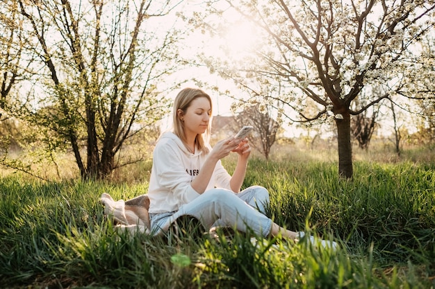 Junge Frau, die im Park sitzt, mit einem Smartphone