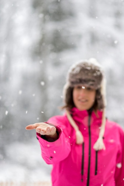 Junge Frau, die im Schnee steht und ihren Arm vor sich ausstreckt, um Schneeflocken zu fangen