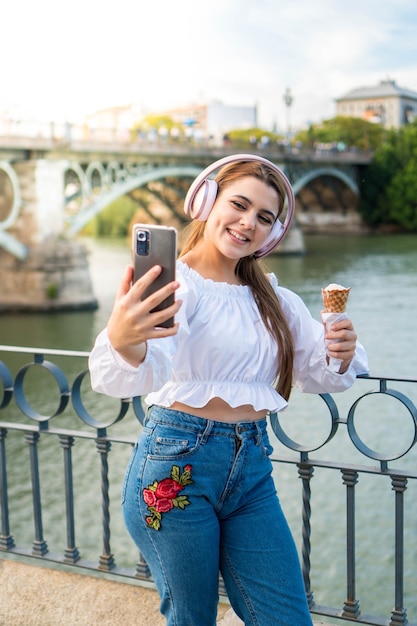 Junge Frau, die im Sommer Musik hört, ein Eis im Freien isst und ein Foto macht