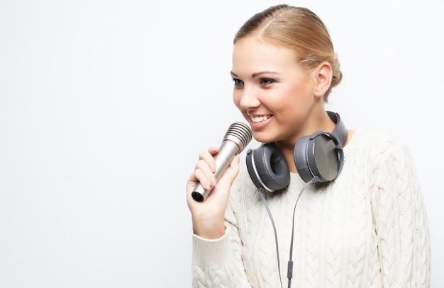 Junge Frau, die im Studio auf weißem Hintergrund mit Kopfhörern ins Mikrofon singt