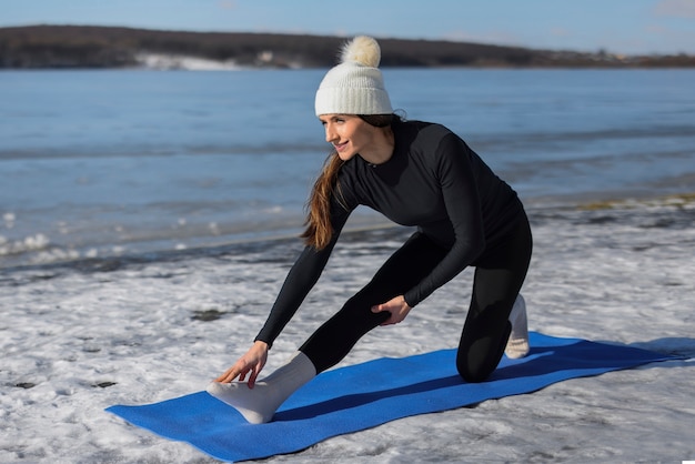 Junge Frau, die im Winter am Strand Yoga im Freien praktiziert