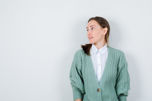 Junge Frau, die in Bluse, Strickjacke und fokussiertem Blick beiseite schaut. Vorderansicht.