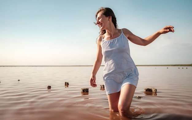 Junge Frau, die in den roten See geht Sexy glückliches Mädchen im gestreiften weißen Kleid, das lächelt und wegschaut