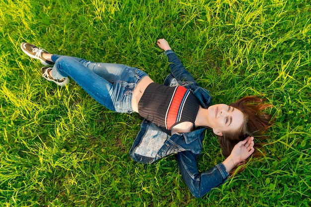 Junge frau, die in der natur auf grünem gras im park liegt, entspannt ihr rotes lächeln