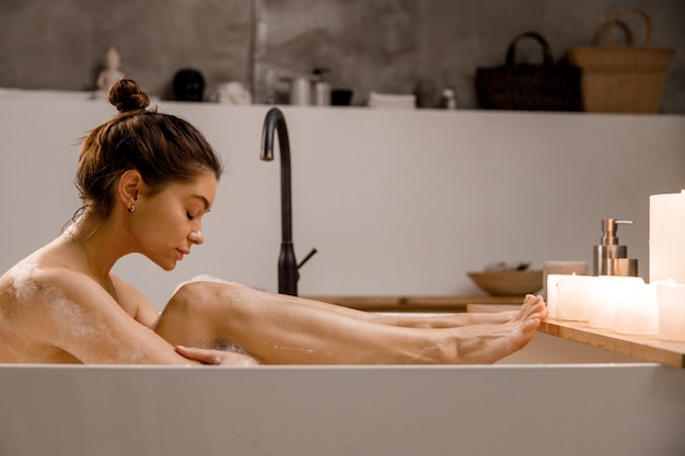 Junge Frau, die in der schönen Vintagen Badewanne voller Schaum im Retro-Badezimmer verziert entspannt