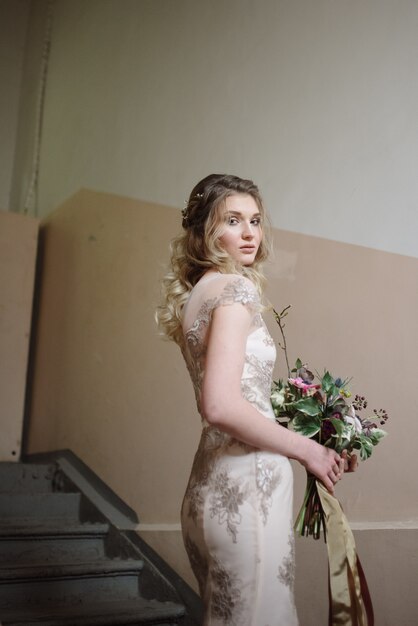 Junge Frau, die in einem hellen langen Spitzenkleid mit einem Blumenstrauß in ihren Händen aufwirft