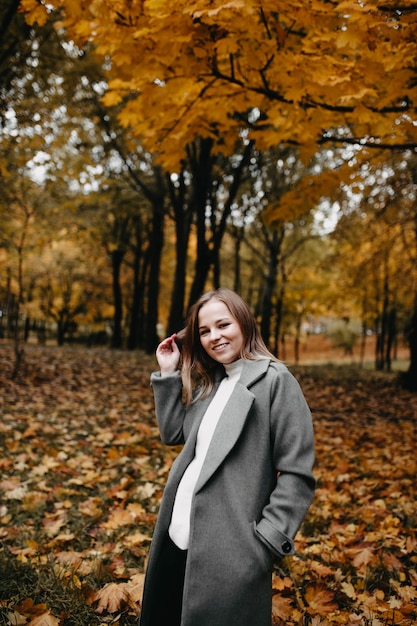 junge Frau, die in einem langen Mantel im Herbstpark spaziert