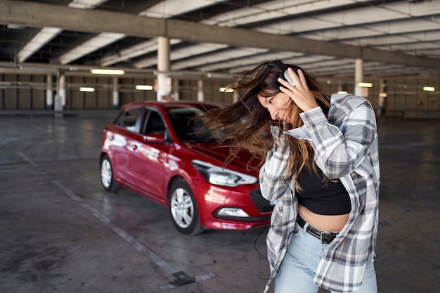 Junge Frau, die in einem Parkplatz tanzt. Sie hört Musik mit Kopfhörern.