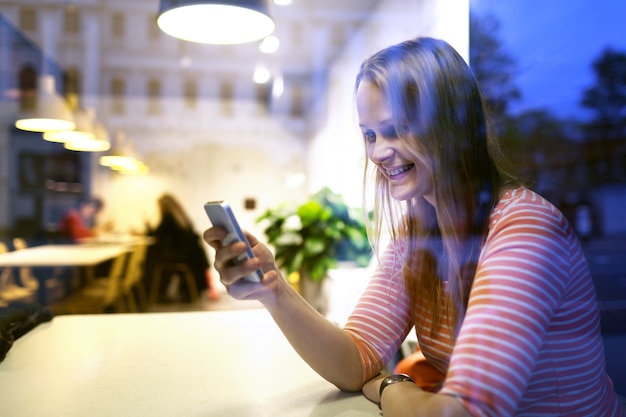 Junge Frau, die in einem Restaurant verwendet Mobile sitzt