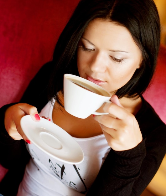 Junge Frau, die in einem trinkenden Kaffee des Cafés sitzt