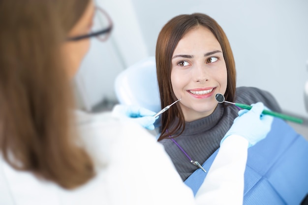 Junge Frau, die in einem zahnmedizinischen Stuhl lächelt mit den gesunden und weißen Zähnen sitzt.