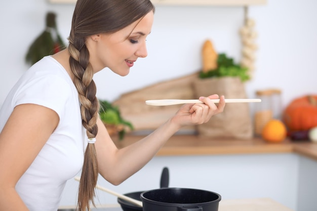 Junge Frau, die in einer Küche kocht Hausfrau, die Suppe durch Holzlöffel schmeckt