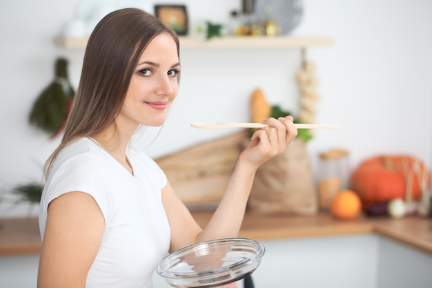 Junge Frau, die in einer Küche kocht Hausfrau, die Suppe durch Holzlöffel schmeckt