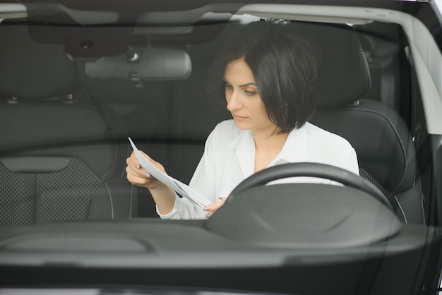 Junge Frau, die in ihrem neuen Auto in einem Ausstellungsraum lächelt