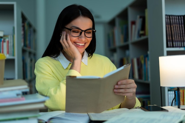 Junge Frau, die Informationen sucht und Bücher auf dem Tisch der Hochschulbibliothek liest, um ihre akademische Ausbildung zu erforschen und weiterzuentwickeln