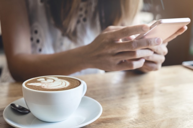 Junge Frau, die intelligentes Telefon in der Kaffeestube verwendet