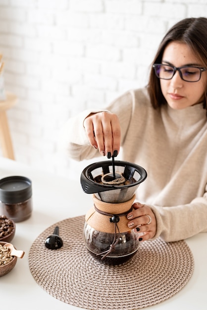 Junge Frau, die Kaffee im Kaffeemacher braut, der heißes Wasser in den Filter gießt