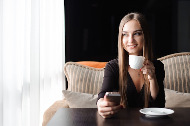 Junge Frau, die Kaffee in einem Café trinkt und ein Handy benutzt.