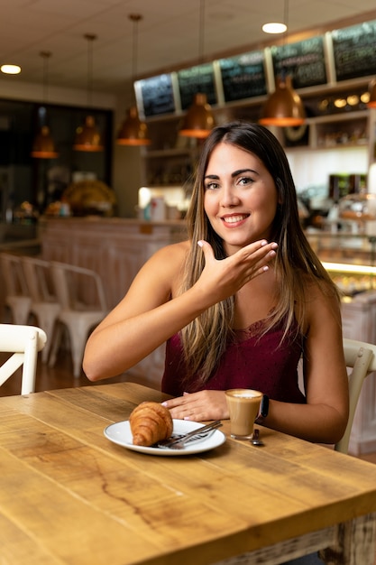 Junge Frau, die Kaffee trinkt und das Zeichen eines Zuhörers macht.