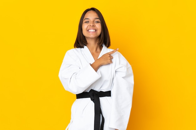 Junge Frau, die Karate lokalisiert auf gelbem Hintergrund zeigt, zeigt auf die Seite, um ein Produkt zu präsentieren