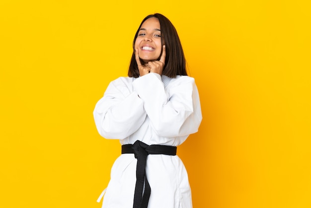 Junge Frau, die Karate lokalisiert auf gelber Wand tut, die mit einem glücklichen und angenehmen Ausdruck lächelt