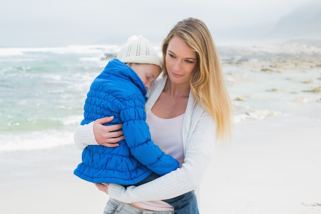 Junge Frau, die kleines Mädchen am Strand trägt