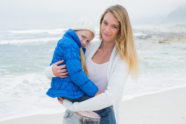 Junge Frau, die kleines Mädchen am Strand trägt