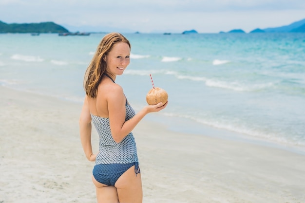 Junge Frau, die Kokosmilch am Strand trinkt