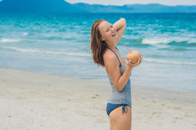 Junge Frau, die Kokosmilch am Strand trinkt