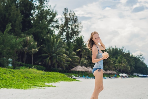 Junge Frau, die Kokosmilch am Strand trinkt.