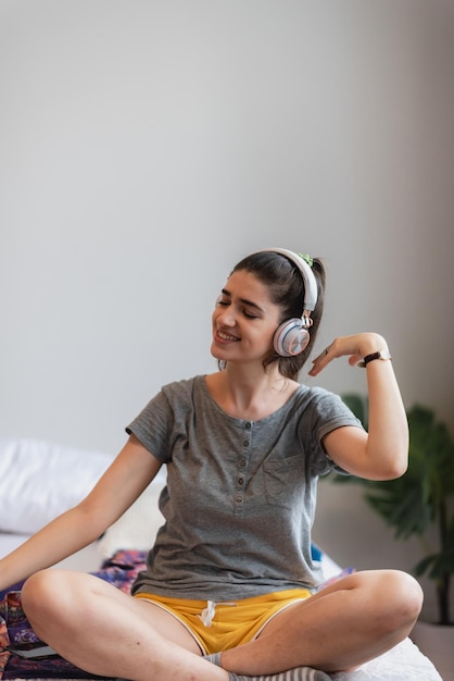 Junge Frau, die Kopfhörer oder Kopfhörer trägt, um sich mit Lied auf dem Bett im Schlafzimmer zu Hause zu entspannen