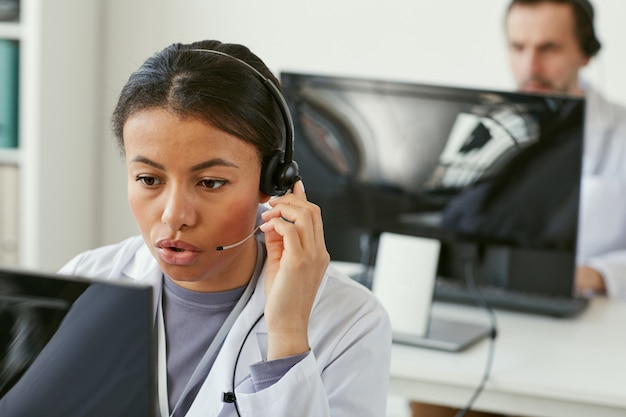 Junge Frau, die Kopfhörer trägt, die am Computer arbeiten, den sie auf Anrufen im medizinischen Callcenter beantwortet